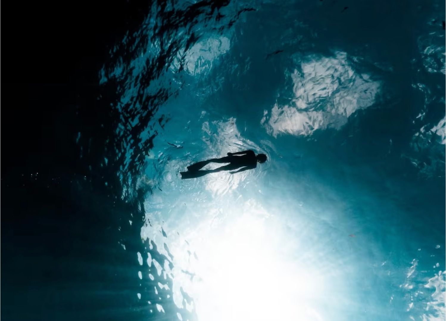 A lone freediver silhouetted against the surface light, seen from the deep ocean below